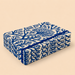 A stack of rectangular boxes wrapped in cream fabric printed with a bold blue coral or branch-like pattern, tied with a matching blue ribbon, on a plain beige background.