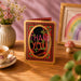 Decorative 'Thank You' card on a wooden table with a cup of tea, flowers, and a rainbow picture frame.