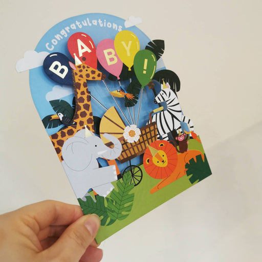 Colorful baby shower card with animals and balloons held by a hand on a light background