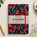 A floral A5 notebook with a navy blue background, red poppy pattern, and a cream paper band label reading 'Alleyjoy Design Ltd A5 NOTEBOOK'. The notebook is styled in a flat-lay on a light beige surface with a gold pen, white baby's breath flowers, and green leaves.