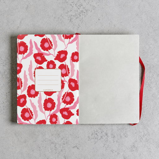 An open notebook with a white cover decorated with a red and pink floral pattern, featuring a blank name label on the front and a red ribbon bookmark, set against a textured gray background.