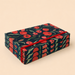 A stack of rectangular notebooks or booklets with a dark navy blue cover featuring a red poppy and green leaf pattern, bound together with a red elastic band, set against a solid beige background.