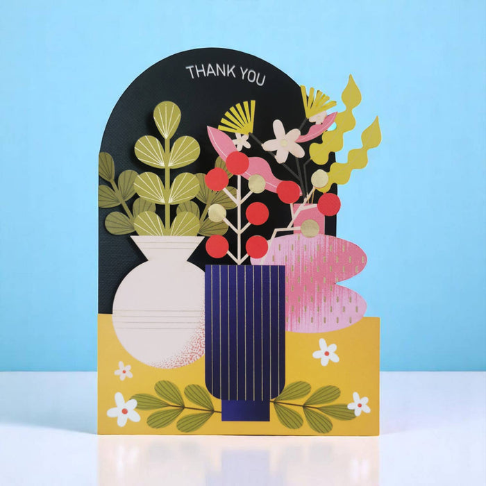 A colorful layered paper card with a 3D floral arrangement in vases, featuring the words 'THANK YOU' at the top, set against a light blue background.