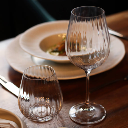 Two clear wine glasses on a wooden table with a blurred plate of food in the background.