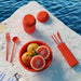 Red outdoor dining set with fruit on a stone surface by water