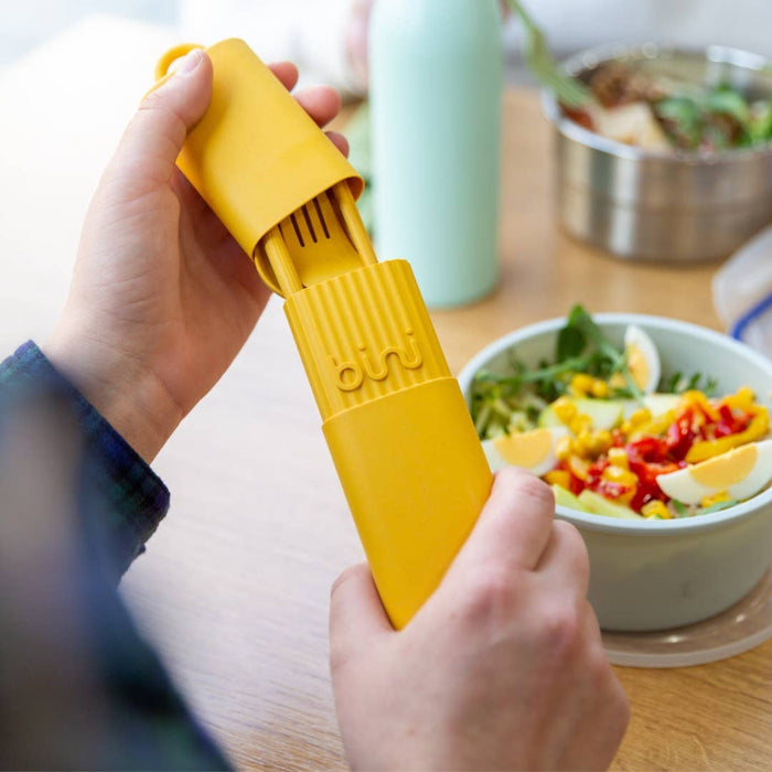 Yellow cutlery set being opened over a salad on a wooden table