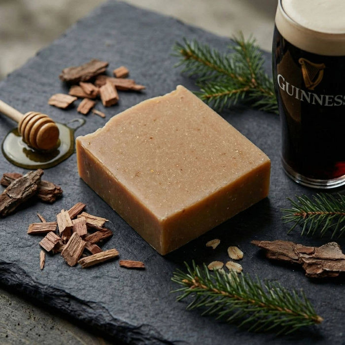 Bar of soap on a dark slate surface with a pint of Guinness beer, honeycomb, and pine branches.