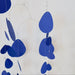 A minimalist metal wire hanging mobile with irregular blue paper cutouts, suspended against a plain off-white wall.