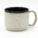 A ceramic mug with a light sage green exterior featuring a raised cream maze pattern, a solid black interior, and a matching sage green handle, shown on a white background.