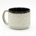 A ceramic coffee mug with a textured, raised maze-like pattern in cream and light gray, featuring a solid black interior and a matching light gray handle, set against a plain white background.