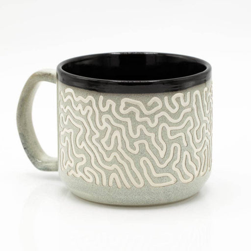 A ceramic coffee mug with a textured, raised maze-like pattern in cream and light gray, featuring a solid black interior and a matching light gray handle, set against a plain white background.