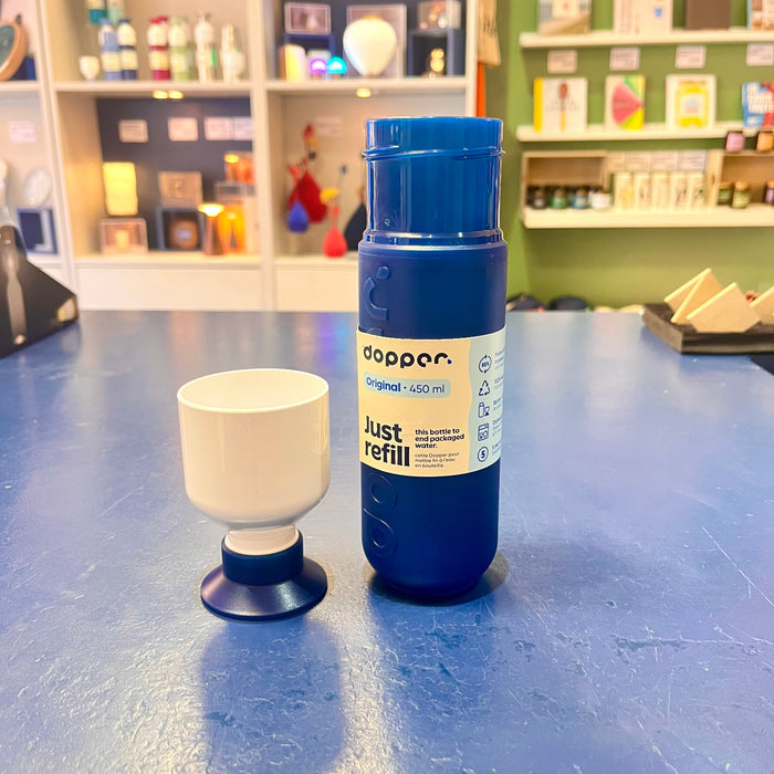 Blue Dopper water bottle and white cup on a blue table with shelves in the background