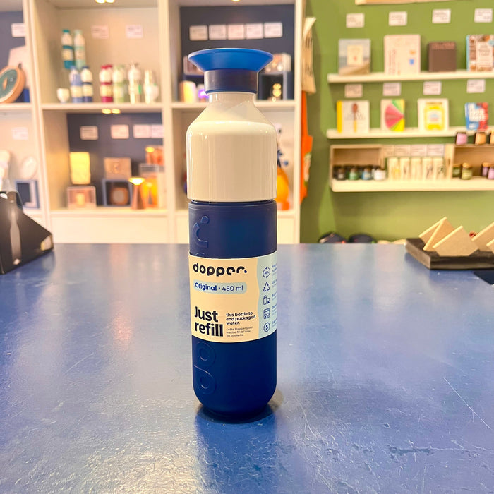 Blue and white Dopper water bottle on a blue table with shelves in the background
