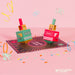 A pop-up cardboard party decoration set featuring two box-like characters labeled CRASH and BANG standing on a circular black and pink base, with colorful confetti and streamers scattered on a pink background. The Clockwork Soldier logo appears in the bottom right corner.