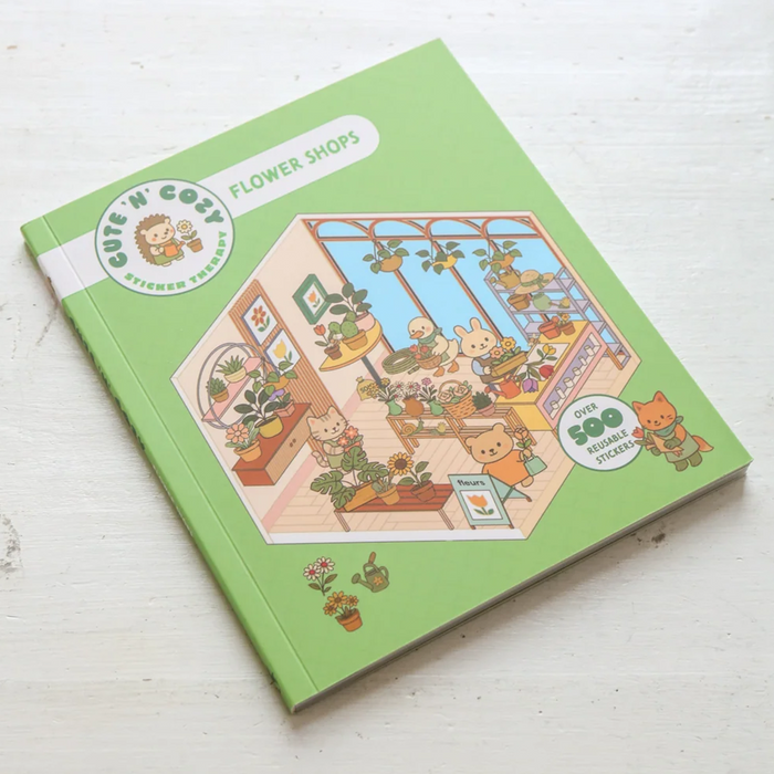 A square green sticker book titled 'Flower Shops' by Cute 'n Cozy, featuring a colorful illustration of a cozy flower shop interior with animals and plants. The book is photographed on a white wooden surface.
