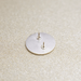 A close-up of the back of a round silver-toned earring, showing two post and butterfly backings, placed on a textured beige surface.