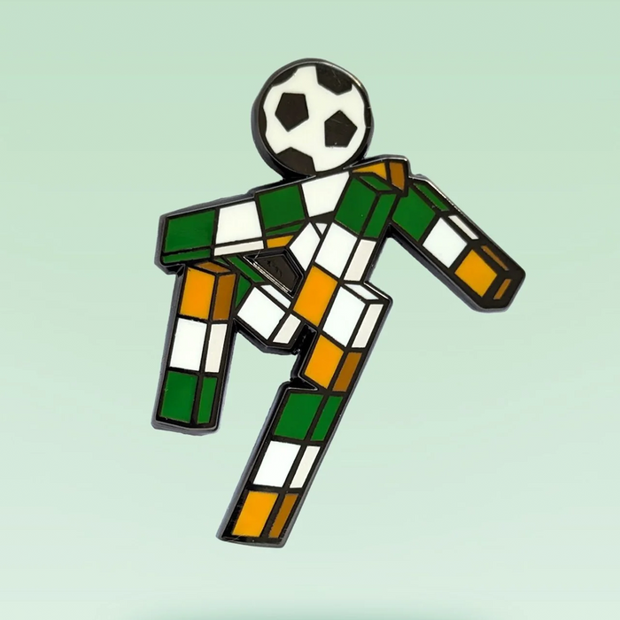 A soccer-themed pin or charm shaped like a stylized player made of green, white, and orange checkered blocks, with a black-and-white soccer ball for a head, shown on a pale green background.