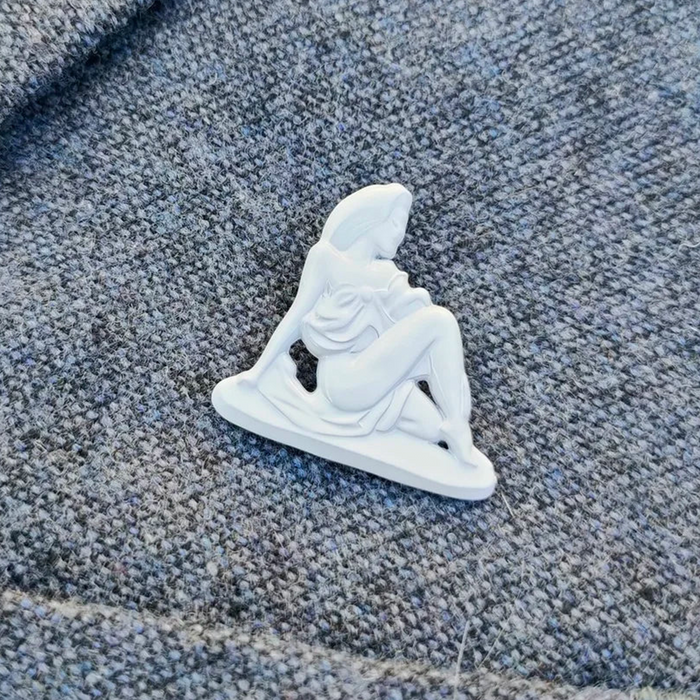 A small white figurine pin or charm shaped like a seated woman, placed on textured gray fabric.