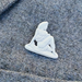 A small white figurine pin or charm shaped like a seated woman, placed on textured gray fabric.