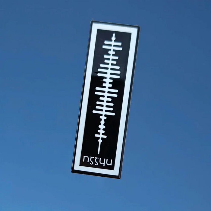 A rectangular black and white sticker or decal featuring a white abstract soundwave-like graphic and the mirrored text 'nssyu' at the bottom, shown against a solid blue background.