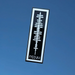 A rectangular black and white sticker or decal featuring a white abstract soundwave-like graphic and the mirrored text 'nssyu' at the bottom, shown against a solid blue background.