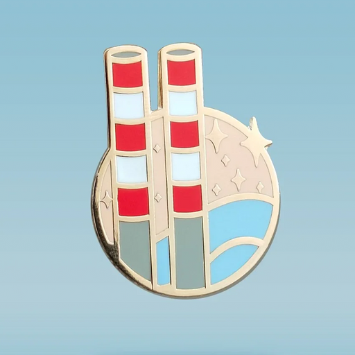 A circular enamel pin featuring a stylized illustration of the poolbeg towers in red and white, with stars and blue water, against a blue background.