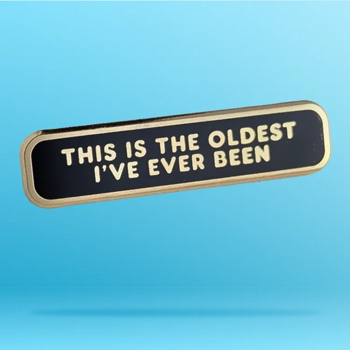 A rectangular enamel pin with rounded corners, featuring a black face and gold-toned border. The text 'THIS IS THE OLDEST I'VE EVER BEEN' is raised in gold lettering.