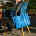 Blue bag hanging off the back of a wooden chair on a patio.