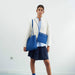 Person wearing a white blazer, blue skirt, and carrying two blue bags against a white background