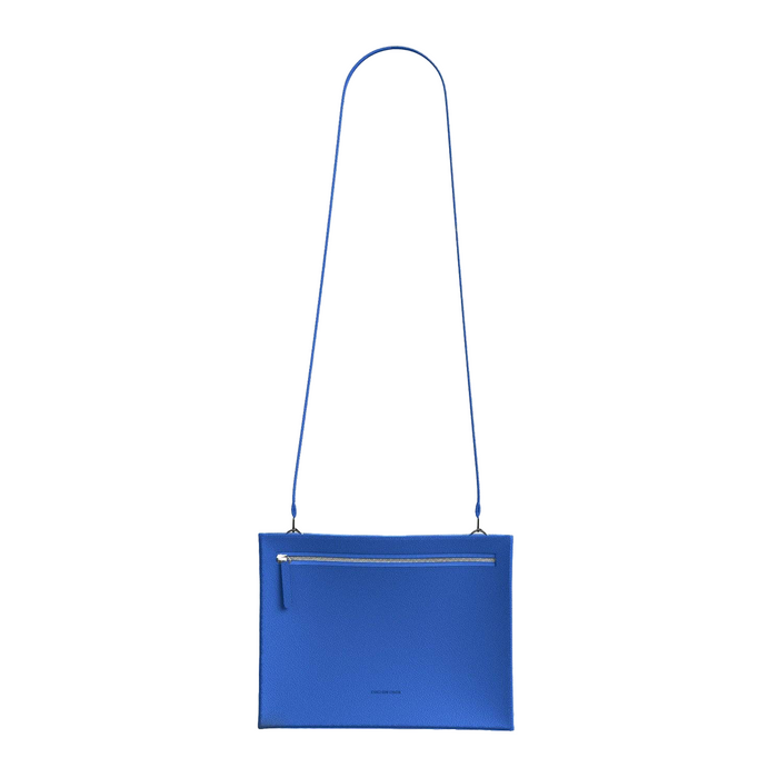 A bright blue leather crossbody bag with a matching blue shoulder strap, a front zippered pocket, and a small embossed logo near the bottom center, shown against a plain white background.