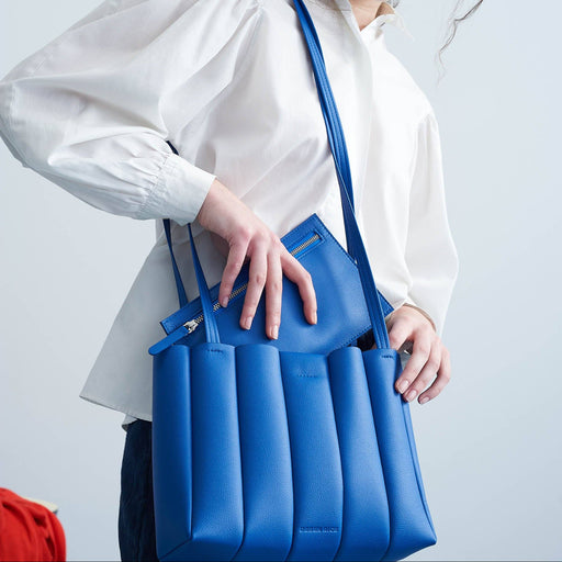 Woman holding a blue handbag against a light gray background
