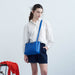 Person wearing a white shirt, blue shorts, and blue shoes, holding a blue bag in a minimalistic setting.