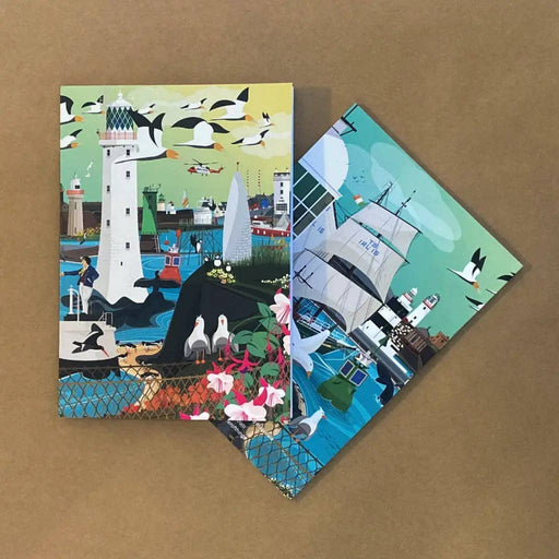 Two illustrated notebooks featuring a lighthouse and coastal scene on a brown background.