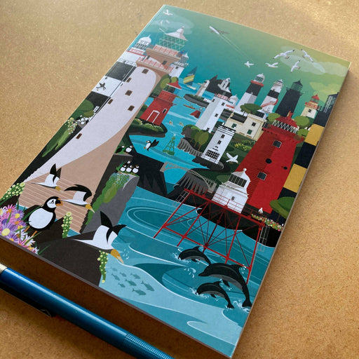 Notebook with a colorful illustration of a coastal scene featuring buildings, penguins, and dolphins on a beige surface.