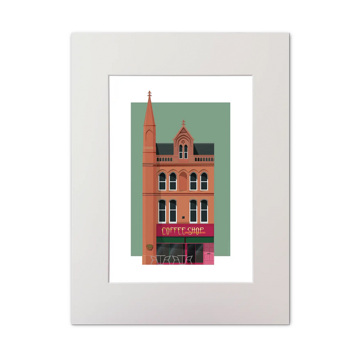 A framed art print featuring a stylized illustration of a brick coffee shop building against a sage green background, presented in a white frame with a white mat.