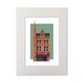 A framed art print featuring a stylized illustration of a brick coffee shop building against a sage green background, presented in a white frame with a white mat.