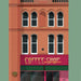 A stylized illustration of a brick building facade with arched windows and a storefront sign reading "COFFEE SHOP" in gold lettering on a magenta background.