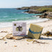 Bar of soap and packaging on a beach with ocean and rocks in the background