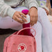 Person holding a pink bottle with a white cap next to a pink backpack featuring a logo.