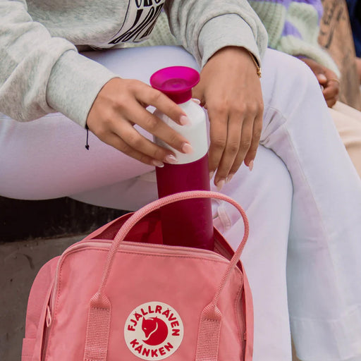Person holding a pink bottle with a white cap next to a pink backpack featuring a logo.