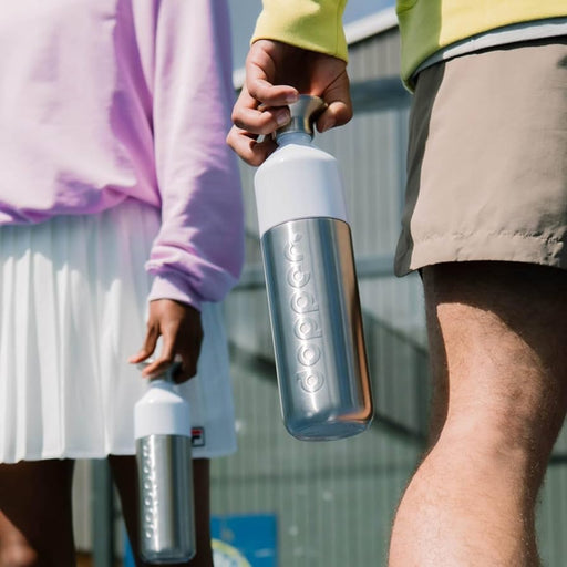 Two people holding silver dopper water bottles outdoors with a blurred background
