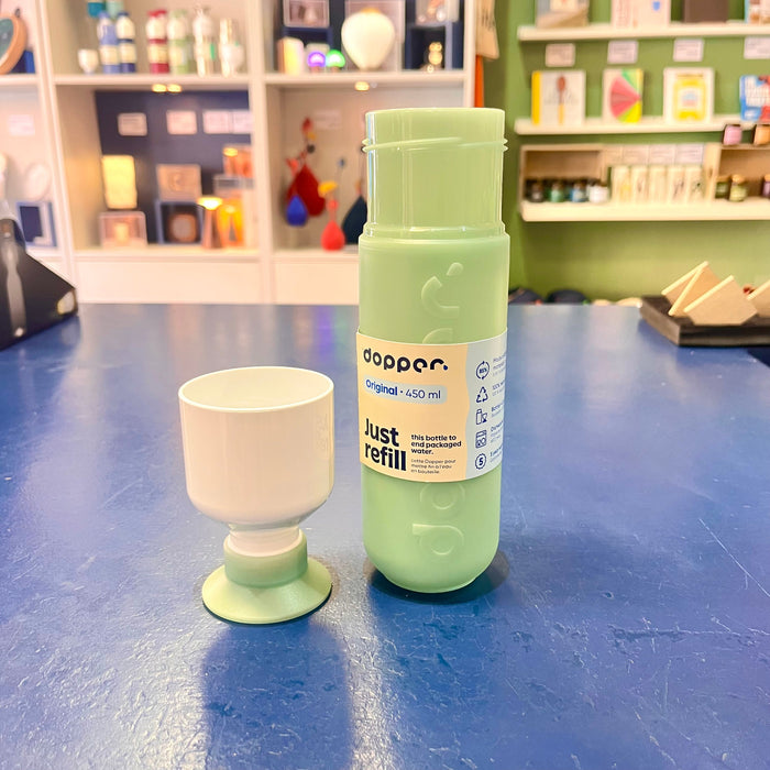 Mint green refillable water bottle and cup on a blue surface with a store shelf in the background.