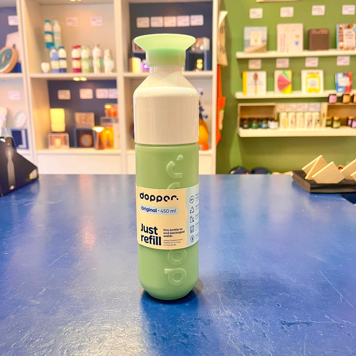 Mint green and white water bottle with 'dopper' branding on a blue surface, store shelves in the background.