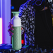 Person holding a green and white bottle with electronic equipment in the background