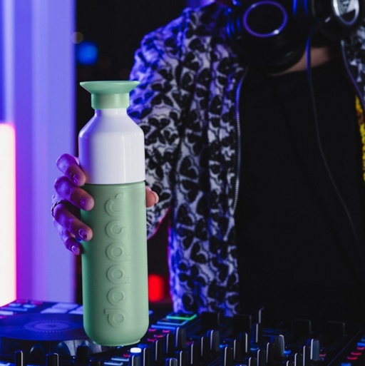 Person holding a green and white bottle with electronic equipment in the background