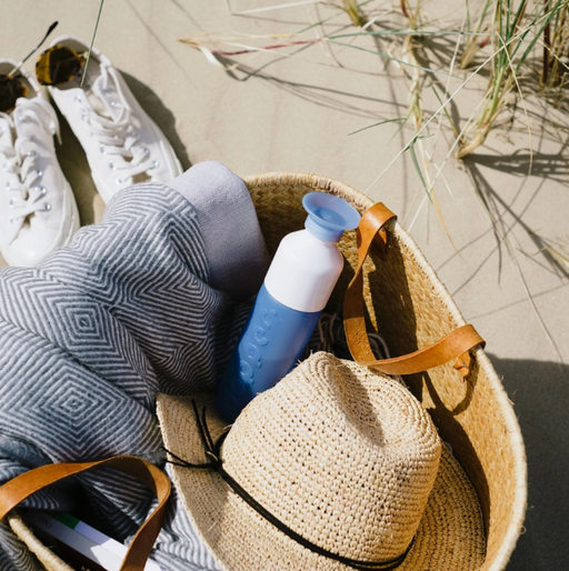 Wicker bag with a straw hat, towel, and blue bottle on sand