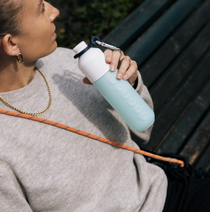 Person holding a light blue water bottle with a white cap outdoors.