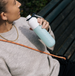 Person holding a light blue water bottle with a white cap outdoors.