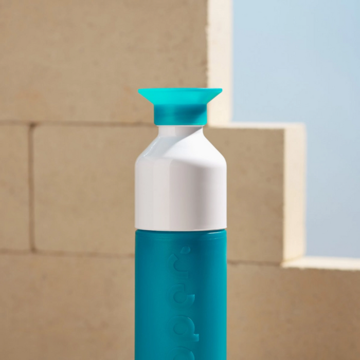 Teal and white bottle with a blue cap against a beige wall.