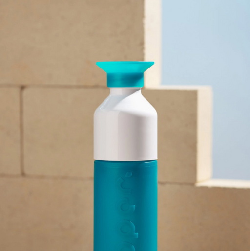 Teal and white bottle with a blue cap against a beige wall.